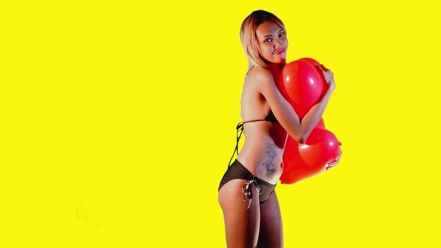 Pinoy girl standing in front of a yellow background sways with two heart shaped balloons held tightly against her body.
