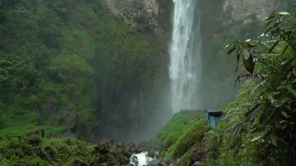 Vertical pan shot in slo-mo of a woman looking up at Sipiso Piso waterfall in North Sumatra, Indonesia. - Powered by Adobe