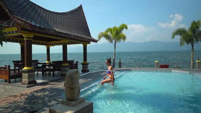 Woman walking out of a pool at a picturesque resort on Lake Toba in North Sumatra, Indonesia. 60fps.