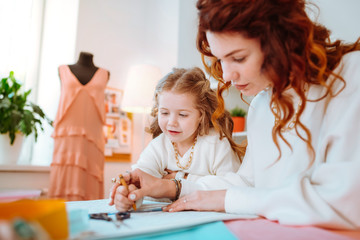 Obraz na płótnie Canvas Appealing cute girl standing near mother designing dresses