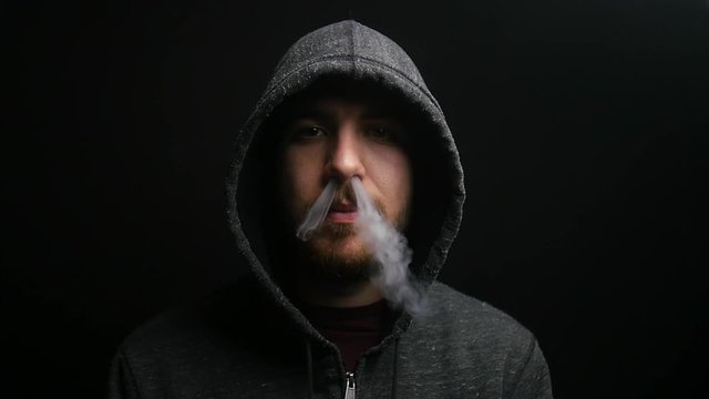 Hooded man exhales vapor through his nose in slow motion.