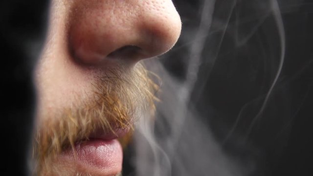 Man exhales vapor through his nose.