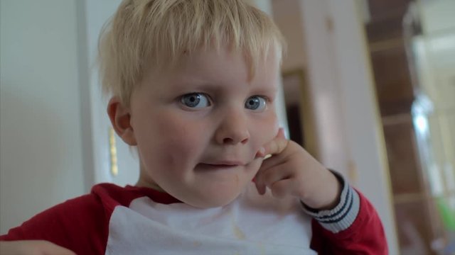 A cute child with blonde hair and blue eyes pulling a smile with his fingers. CLOSE UP.