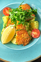 Breaded chicken with vegetables and herbs on a blue plate. Dark wooden background. Restaurant food.