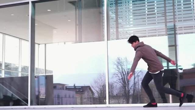 Young parkour athlete doing a cork in front of a glass wall in slow motion