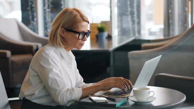 Senior businesswoman in elegant clothing is working with laptop in cafe typing looking at computer screen focused on work. People, business and career concept.