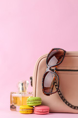 Stylish fashionable pink bag and French macaroons and perfume cakes, glasses on a bright trendy pink background. female accessory concept.