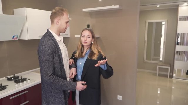 Caucasian Married Couple Standing in Kitchen of New Real Estate Apartment Property Talking and Looking While Male Realtor Broker Making Phone Call in Other Room. Light Camera Movement