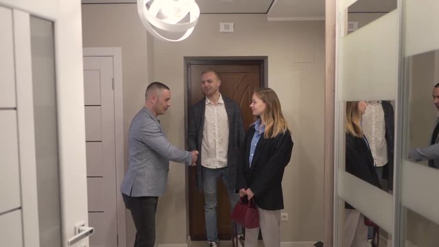 Realtor Real Estate Broker Opens The Door To Potential Couple Buyers of New Apartment Property and They Going In. Light Pull Back Camera Movement