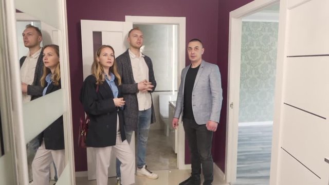 Young Married Caucasian Couple Standing With Realtor Real Estate Broker in Lobby of New Apartment Property and They Talking. Light Camera Movement