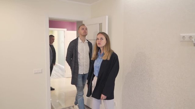 Caucasian Married Couple Going In New Empty Finished Real Estate Property With Realtor and Looking Around. Light Camera Movement