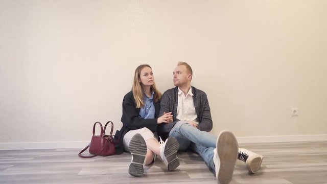 Young Caucasian Married Couple Sitting on Floor in New Real Estate Apartment Property And They Talking About Arragement. Light Camera Movement