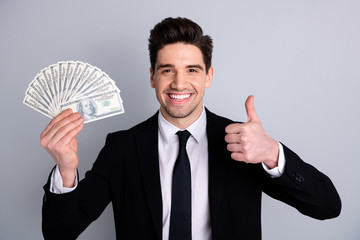 Close-up portrait of nice attractive cheerful guy sales manager financier banker economist holding in hand currency lottery credit loan showing thumbup isolated over light gray background