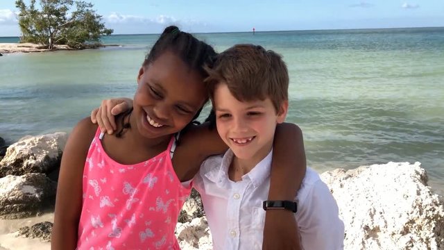 Young African American girl and caucasian boy hugging and smiling on beach