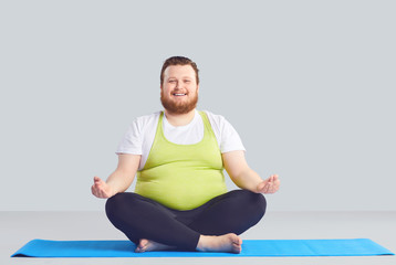 Positive fat man Yogi does yoga exercises a gray background.