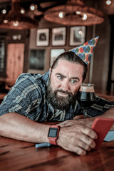 Confused strong man with a beard looking at his phone.