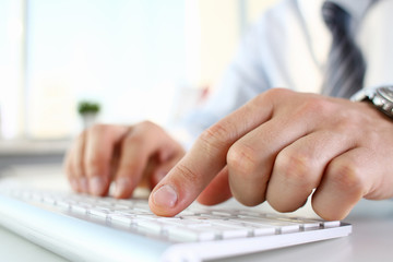Male arms in suit typing on white keyboard using computer pc at office workplace closeup. Accountant finger job modern lifestyle web search assistant enter account login password and note credential