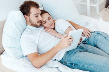 Obraz na płótnie Canvas Happy couple lying on bed and using digital tablet
