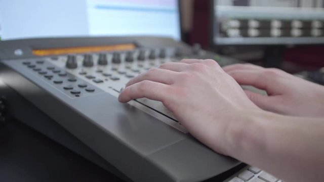 Slow push in on a sound mixers hands as he adjusts levels on the mixboard