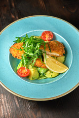 Breaded chicken with vegetables and herbs on a blue plate. Dark wooden background. Restaurant food.