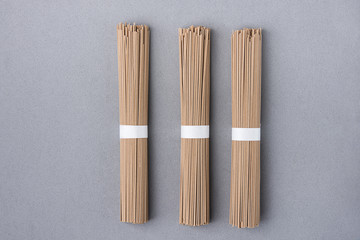 Bundles of Thin Soba Noodles Tied with White Paper Ribbon on Grey Background. Japanese Cuisine New Years Eve Dish. Clean Minimalist Style. Flat Lay. Copy Space