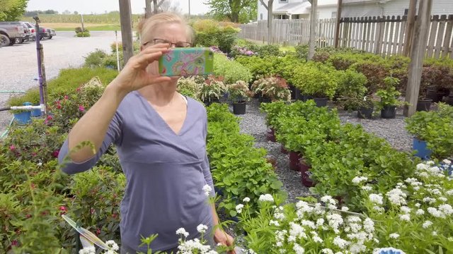 Mature woman using smartphone taking photos of potted plants.