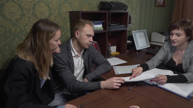 Young Caucasian Married Couple Exploring Documents in Office With Realtors Who Explains Them Contract. Light Camera Movement
