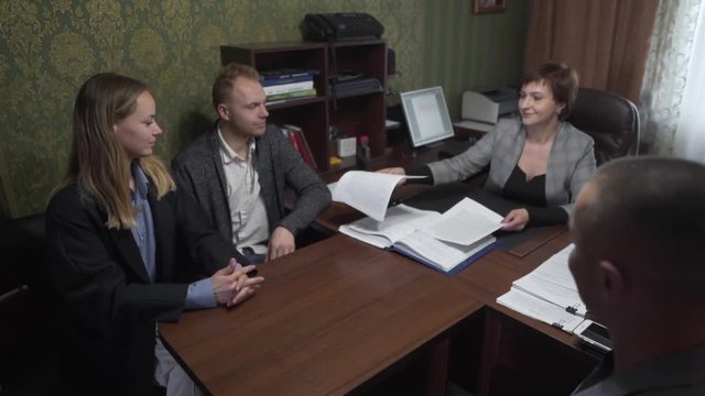 Realtor And Real Estate Brokers Sitting in Office With Caucasian Couple Buyers of New Property and They Give Them Contract Documentation. Light Camera Movement