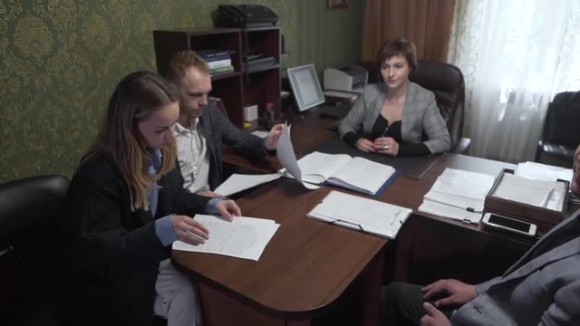 Caucasian Couple Sitting In Realtors Office With Real Estate Broker and Exploring Documentation in Contract for New Property. Light Camera Movement