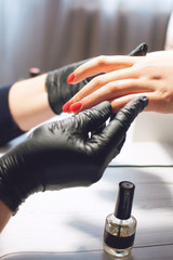 Manicure specialist in black gloves cares about hands nails. Manicurist paints nails with red nail polish.  Manicure beauty salon
