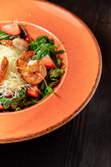 Fresh salad of arugula, shrimp and strawberry. Dark wooden background. Restaurant menu