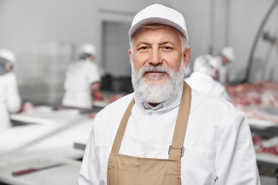 Professional butcher, elderly man in white uniform posing.