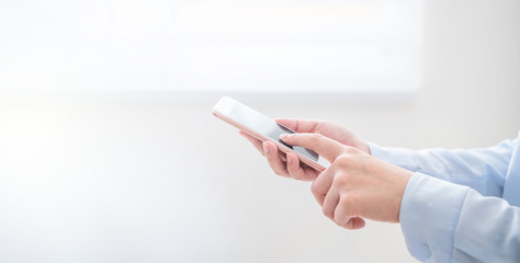 Side view of asia young business woman in blue shirt dress standing beside window and using smart phone in bright office room, copy space, close up