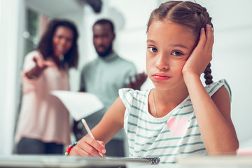 Face portrait of girl doing lessons when her parents talking