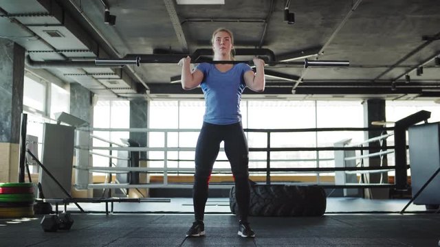 Wide shot of strong female athlete lifting barbell and doing clean and jerk exercise during cross training in gym