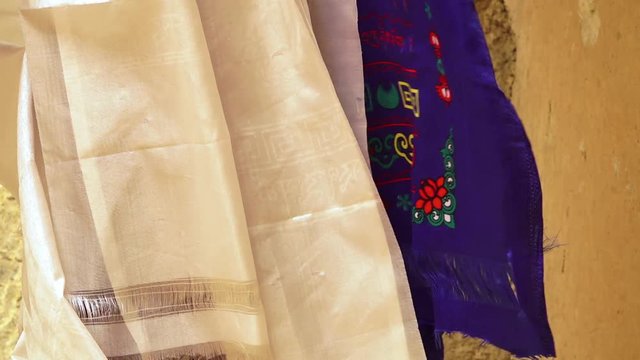 Extreme close up low-angle still shot of light-textured  blue and white Khata scarfs hang on a string at Mulbekh monastery, blown by wind.