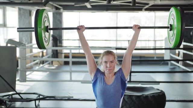 Tilt up of strong female athlete wearing weightlifting belt and knee supporters doing clean and jerk exercise during cross training in gym