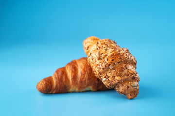 Photo of fresh golden croissants covered sunflower seeds and sesame captured on blue background.