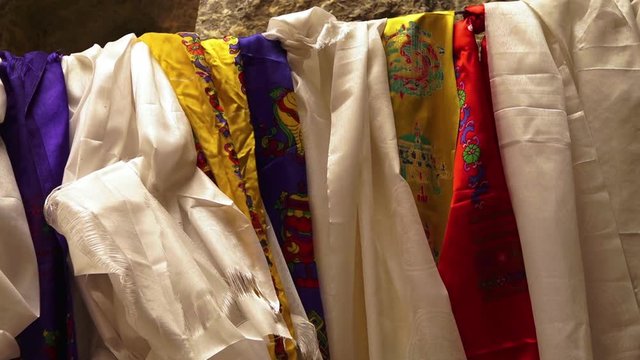 Extreme close up still shot of Khata scarfs in white, yellow, blue, and red colours hanging on a horizontal string, Mulbekh.