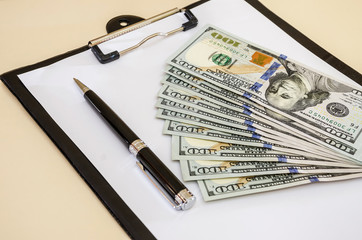 Dollars, pen and white sheet of paper on the background of the table. Close-up.