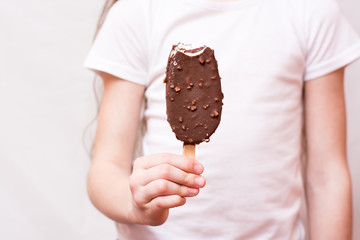 The girl holds in her hand a bitten popsicle in chocolate icing with nuts