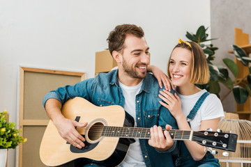 smiling man playing acoustic guitar to wife at home