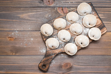 Raw dumplings ready for cooking lie in rows on a wooden cutting board on the table. Top view. Copy space