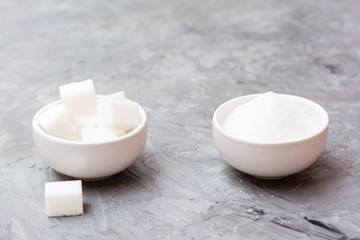 Sugar cubes and granulated sugar in white bowls on a table. Concept