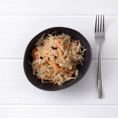 Fermented cabbage. Traditional russian appetizer sauerkraut with carrot in craft plate on white wooden table.