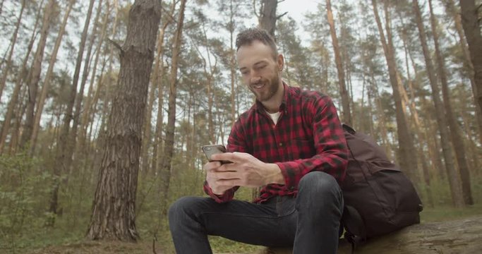 Traveller bearded man using smartphone app while relaxing in the forest