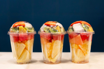 Three mixed fruit vitamin salad in the plastic glass ready to takeaway. Kiwi, pineapple,...