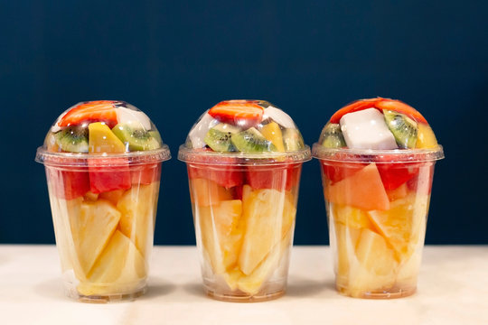 Three mixed fruit vitamin salad in the plastic glass ready to takeaway. Kiwi, pineapple, watermelon, coconut, strawberry, mango in plastic container. Copy space.