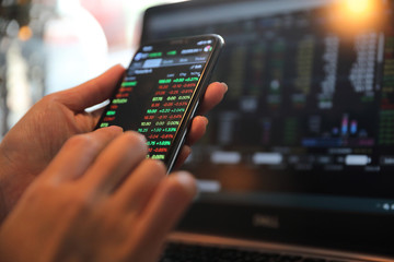 Female hand with smartphone trading stock online in coffee shop , Business concept