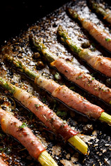 Grilled green asparagus wrapped in ham with the addition of aromatic herbs and spices, top view, close-up